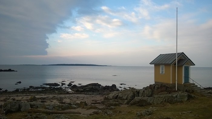 Ett gult hus vid kusten i Skåne med klippor och hav i bakgrunden under en molnig himmel.