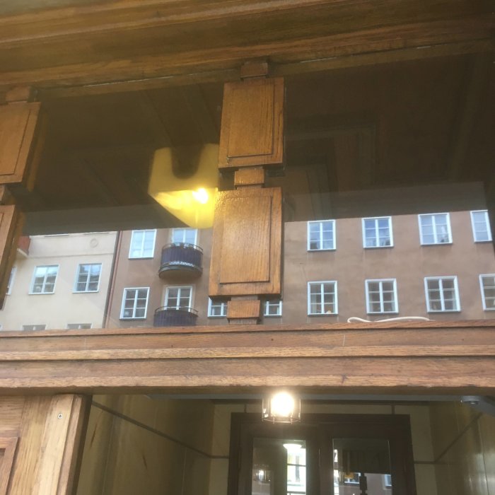 Detaljbild av en överljusbåge i trä med genomtänkt tappkonstruktion, reflekterar stadsmiljö och byggnad genom fönstret.