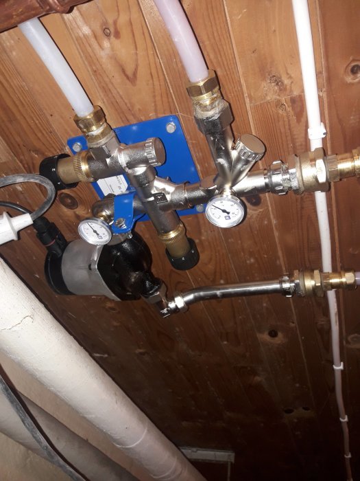 VVS-installation med kopparledningar, rörmokarkopplingar och mätare under taket.