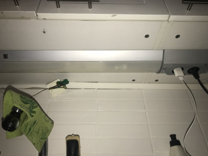 Öppet eluttag under köksskåp bredvid en armatur och utanpåliggande uttag med en stickkontakt.