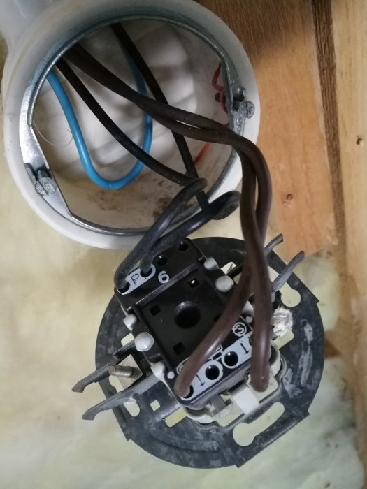 Gammal strömbrytare med svart fas in-kabel och två bruna ut-kablar i ett 70-talshus under renovering.