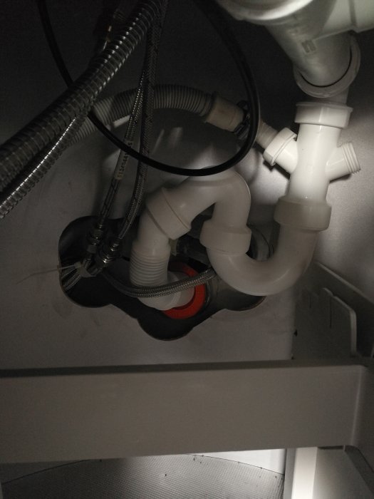 Bild av komplicerad vattenlåsinstallation under köksskåp med anslutna avloppsslangar och rörböj.