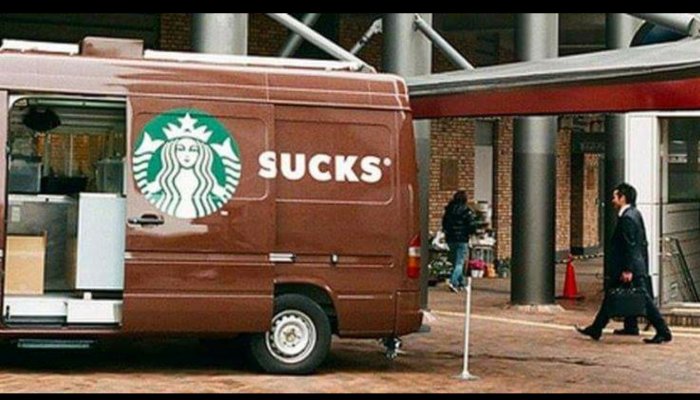 Skåpbil med öppen bakdörr där Starbucks-logo delas så texten "SUCKS" syns.