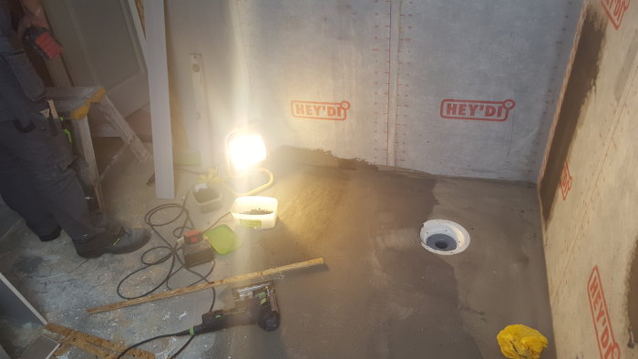 Renoveringsarbete vid golvbrunn, betongytor och verktyg syns, slipning nära väggen.