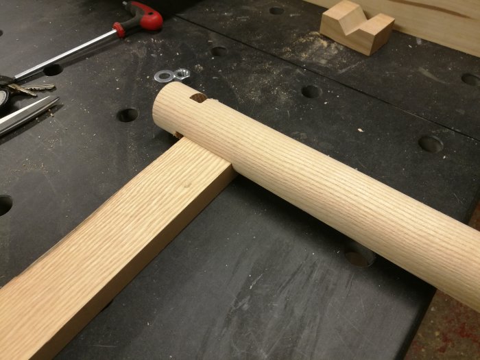 Svarvat träföremål med urfräsningar på arbetsbänk, verktyg och träbitar i bakgrunden.