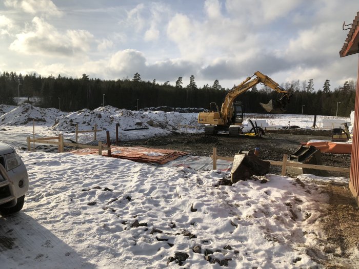 Byggarbetsplats med grävmaskin och fyllnadsmassor i förberedelse för betongplatta.