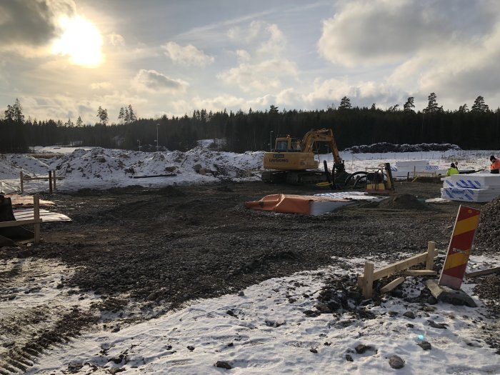 Byggarbetsplats med grävmaskin och fyllnadsmassor, förarbete för grundplatta i soligt landskap.