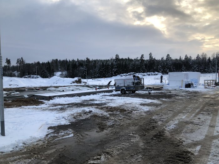 Byggarbetsplats under uppbyggnad med material och utrustning på snötäckt mark.