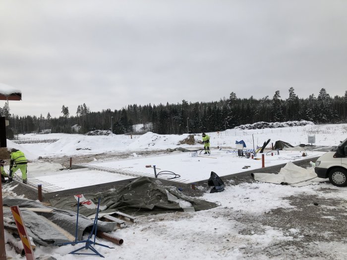 Byggarbetsplats med arbetare som förbereder betongplatta i snöigt landskap.