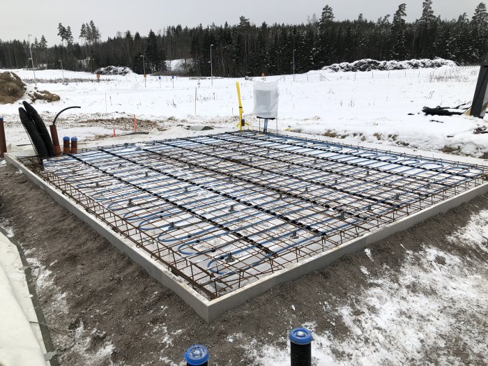 Grundläggning för ett bostadshus med armeringsjärn, förberett för golvvärme och gjutning, i vinterlandskap.