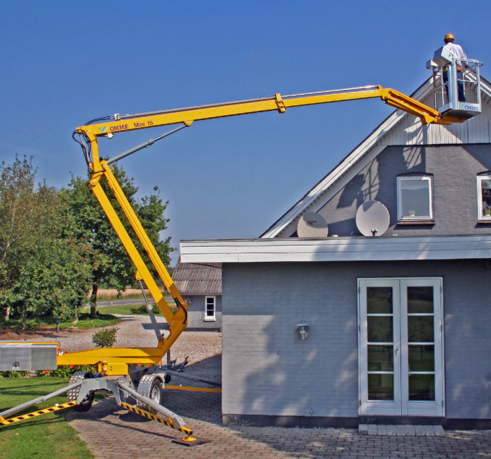 En mobil lift på släp framför ett hus med en person i korgen vid taket.