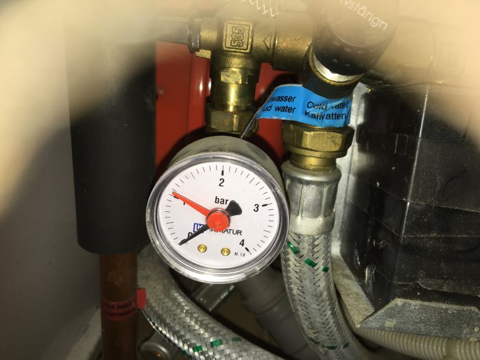 VVS-installation med manometer, märkta rör och ventiler för varmt och kallt vatten.