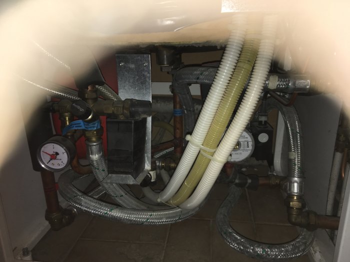 Vy under diskbänk med röranslutningar, mätinstrument, och flexibla slangar synliga i ett husprojekt.