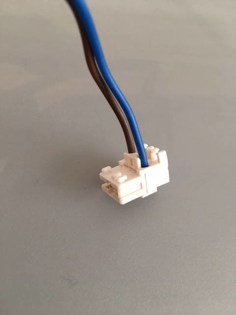 En bild på en elektrisk kontakt med en blå och en brun kabel ansluten, mot en grå bakgrund.