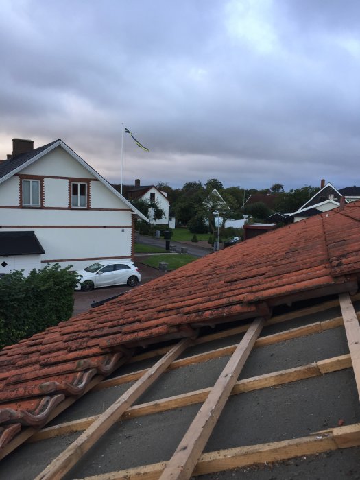 Tak med borttagna takpannor och underarbete inför montering av takfönster på ett bostadshus, med mörka moln i bakgrunden.