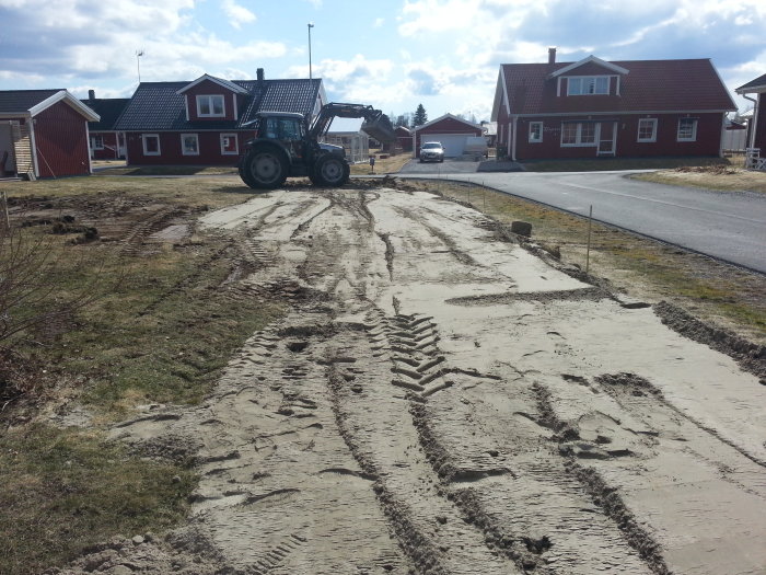 Traktor på ojämn mark med spår efter att ha jämnat ut fyllnadsmassa för gräsmatta.