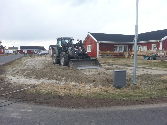 Traktor som jämnar fyllnadsmassa på en tomt i ett bostadsområde under anläggning av gräsmatta.