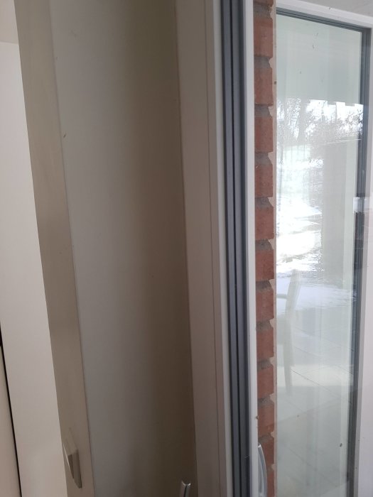 L-formad pelare mellan fönsterdörrar, uppbyggd av tegel och betong, som kan vara en del av husets stödstruktur.