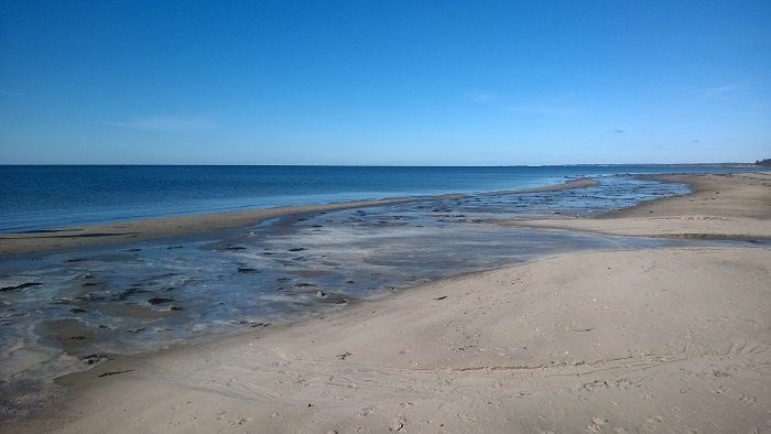 En solig strand med klar blå himmel och havsområden i olika blå nyanser.