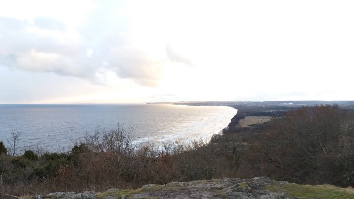 Utsikt över strandkanten vid havet med en ljus himmel vid solnedgång.