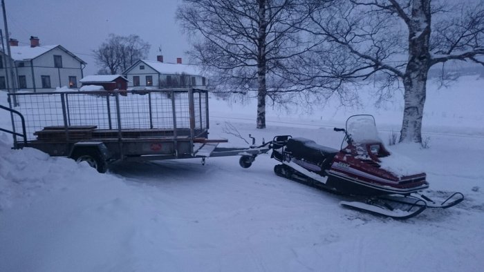 Golvpkankar på släpvagn dragen av en snöskoter i vinterlandskap.