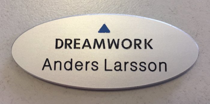 Ovalt namnskylt med texten "DREAMWORK Anders Larsson" och en blå triangel ovanför namnet.