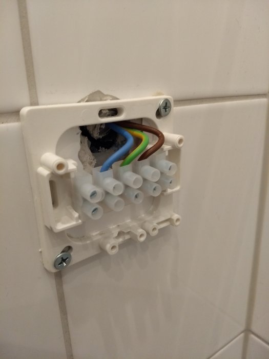 En öppen eldosa med exponerade kablar och tomma kabelskor på en kaklad vägg.