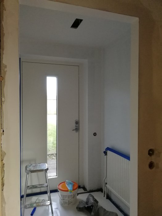 Nymålad vit hall med dörr, stege och målarfärg som tar slut, pågående renovering.