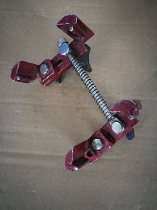 Röd skruvtving med metallspiral på ett brunt underlag.