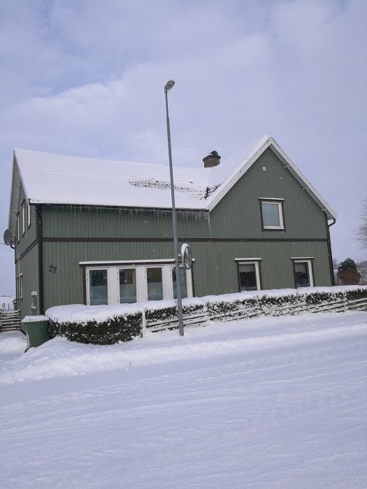 Hus från 1929 med delvis smält snötäckt tak, ny skorstensrör, i vinterlandskap.