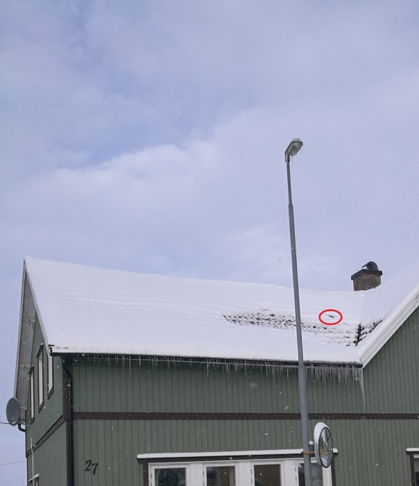 Hus med snötäckt tak och en röd cirkel markerar var ett svart rör går ut.