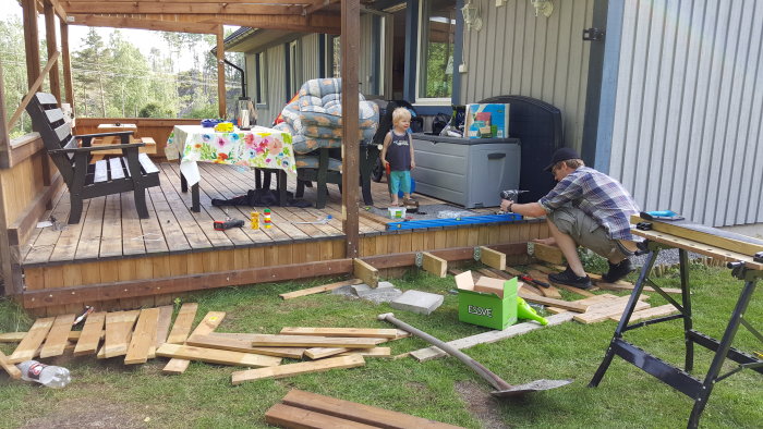 Renovering av trädäck med avlägsnat staket, verktyg och brädor på marken, och en person som arbetar på däcket.