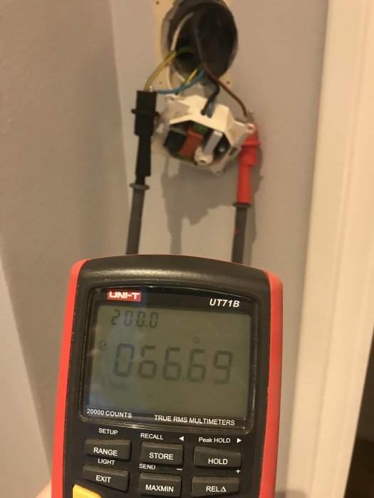 Multimeter visar en resistansmätning på 66.69 ohm framför öppen eldosa med kablar.