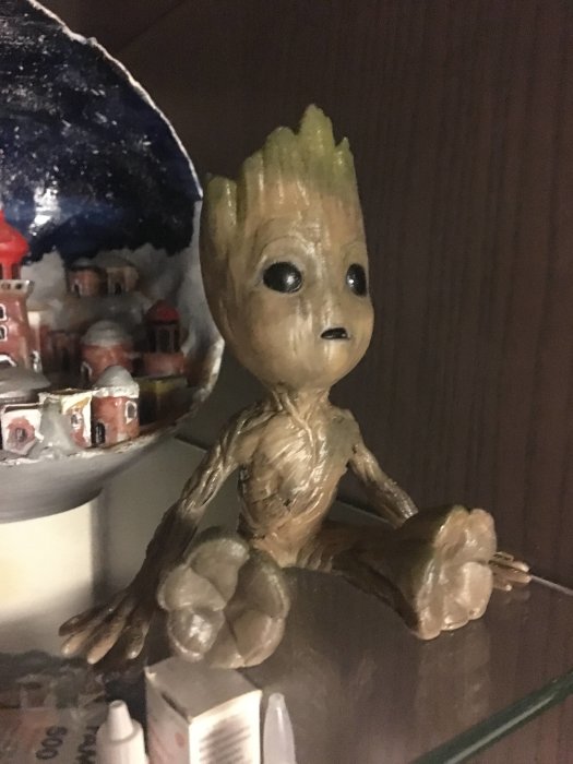Målad 3D-utskrift av figur liknande Groot från Guardians of the Galaxy, uppställd på en hylla.