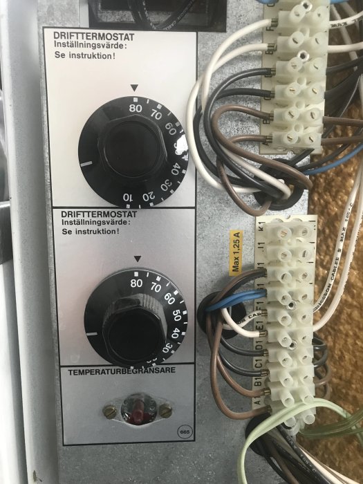 Drifttermostater inställda på elektrisk panel med kablar och instruktionstext.