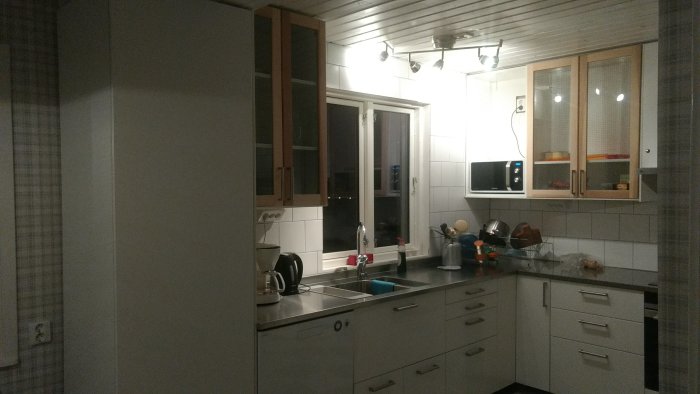 Modernt kök med VEDDINGE vita luckor, TORHAMN vitrinskåp, ORRNÄS handtag och vit kakelvägg.