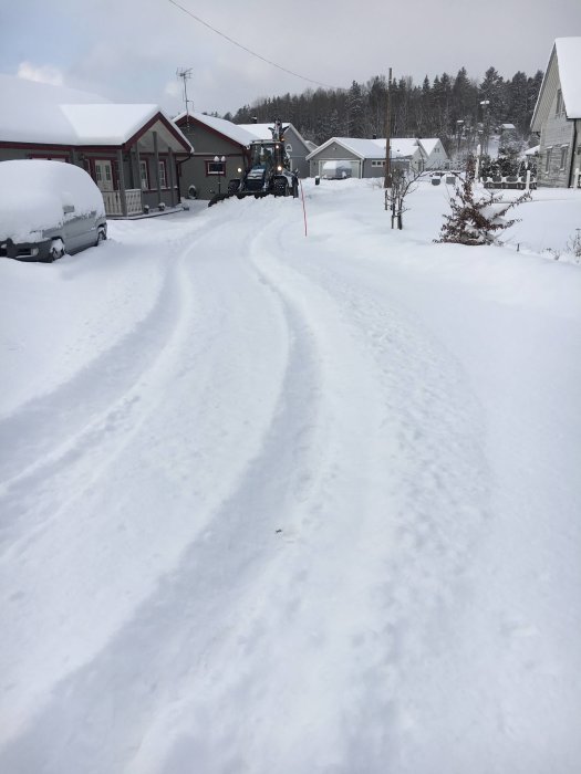 Bild på en snöig uppfart med tydliga spår efter en bil, ett familjehem och en traktor i bakgrunden.