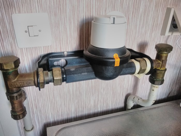Vattenmätarinstallation med avtäckt plats där vred suttit, omgiven av rör och ventiler.