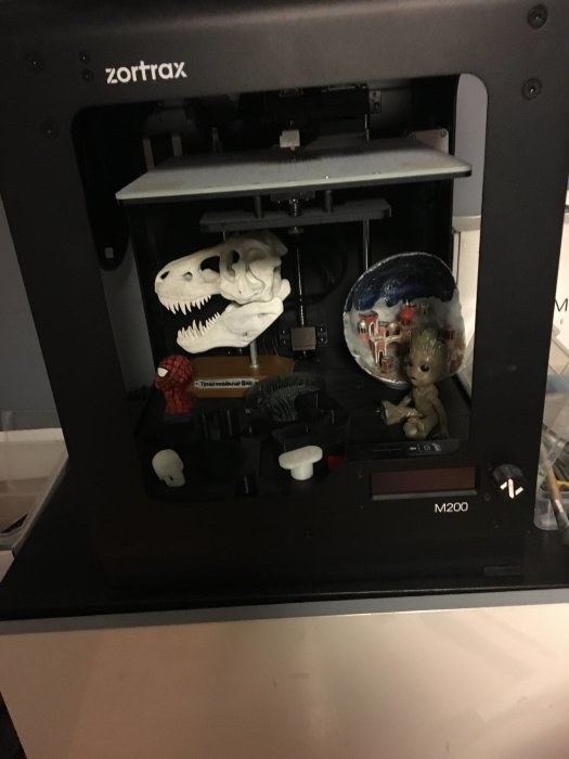 3D-skrivare som skriver ut en dinosaurieskalle, med andra objekt inne i skrivaren.