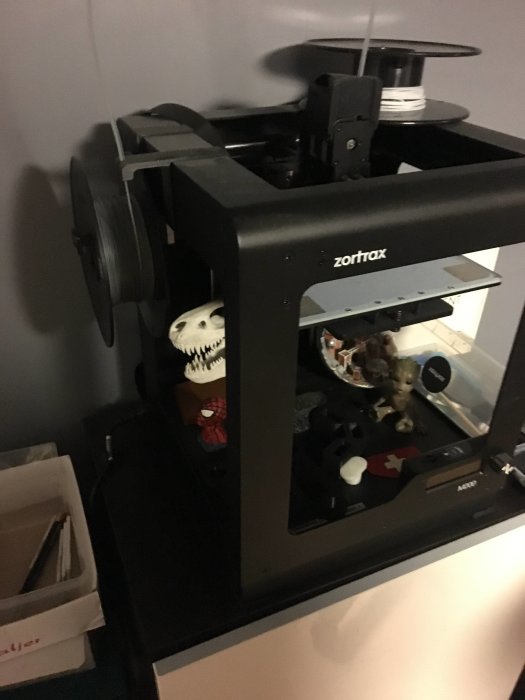 3D-skrivare av märket Zortrax med filamentrullar och leksaksfigurer inuti.