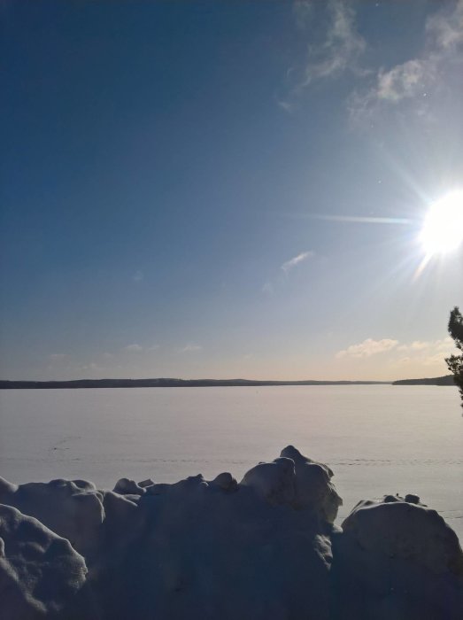 En vinterdag med solsken och snötäckt landskap från ett fönster, klar himmel ovanför ett fruset vatten.