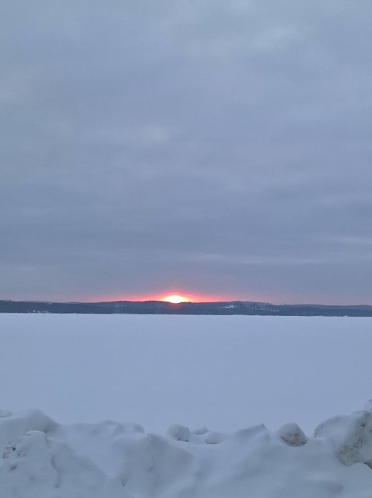 Solnedgång över snöklädd landskap med en glödande sol mellan molnen.