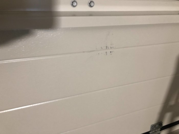 Estetiska skador på en vit, slät garageport med synliga repor och märken.