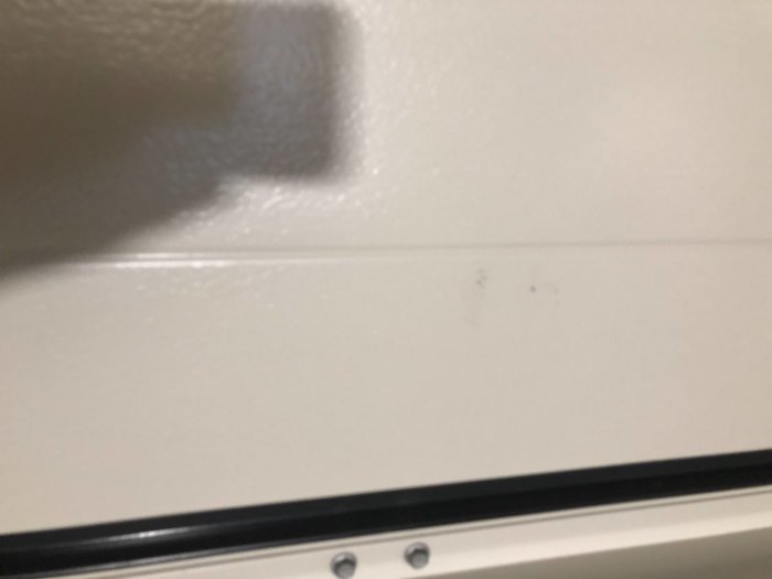Närbild på vit garageport med ytskada och repor mot slät bakgrund.