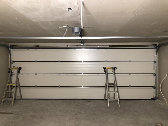 Nyinstallerad vit Hörmann garageport i ett garage, med två stegar och synliga skador på ytan.