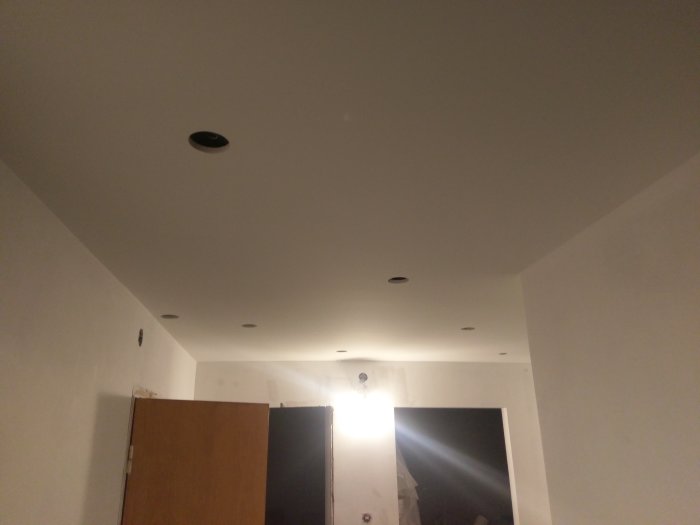 Nymålat tak med infällda spotlights och en väggdel med eluttag under pågående renovering.