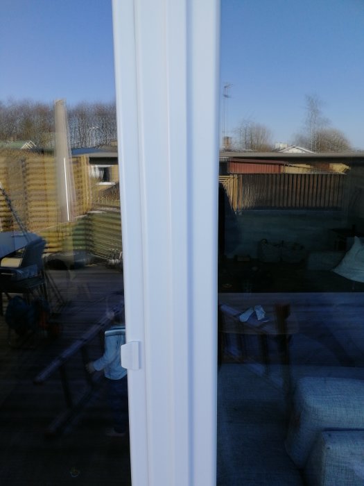 Närbild på en vit fönsterkarm utan synlig kopplingslist, med spegling av en trädgård.