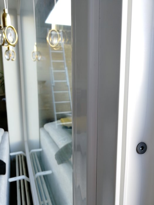 Närbild av två fönsterkarmar utan kopplingslist, synlig skruv och spegling av en trappa och ljuskrona i glaset.