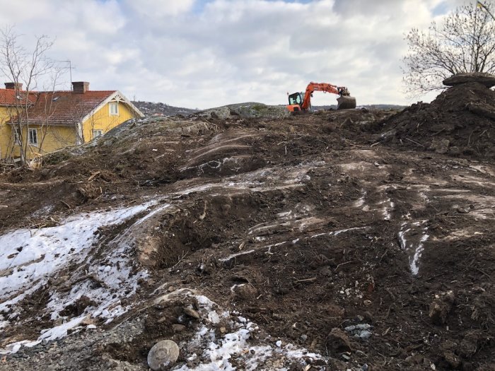 Grävmaskin som arbetar med markberedning på en kylig byggarbetsplats med synligt berg och snörester.
