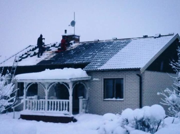 Hus med snötäckt tegelutsida och tak under renovering, arbetare syns montera fönster.